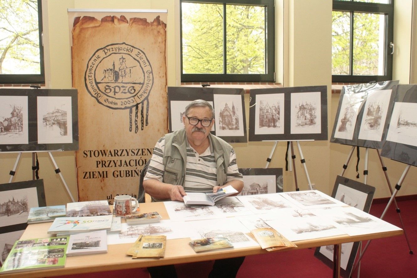 Zdjęcie: Starszy pan siedzący przy stoliku sprzedającym historyczne książki i broszury